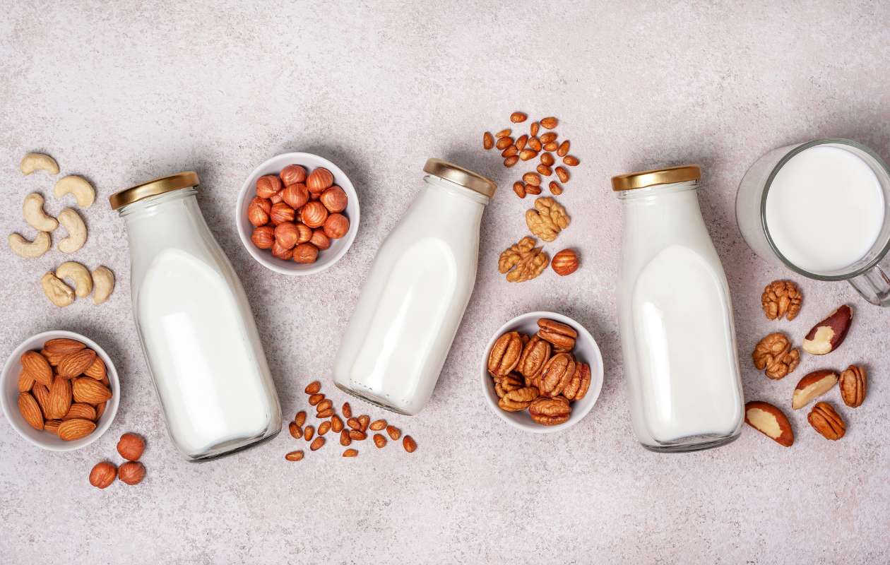Botellas de cristal con diferentes tipos de bebidas vegetales y recipientes con frutos secos sobre un fondo claro, ideal para acompañar café de especialidad.
