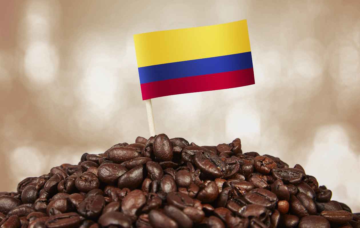 Montón de granos de café tostado coronados con una pequeña bandera de Colombia - Memento Coffee