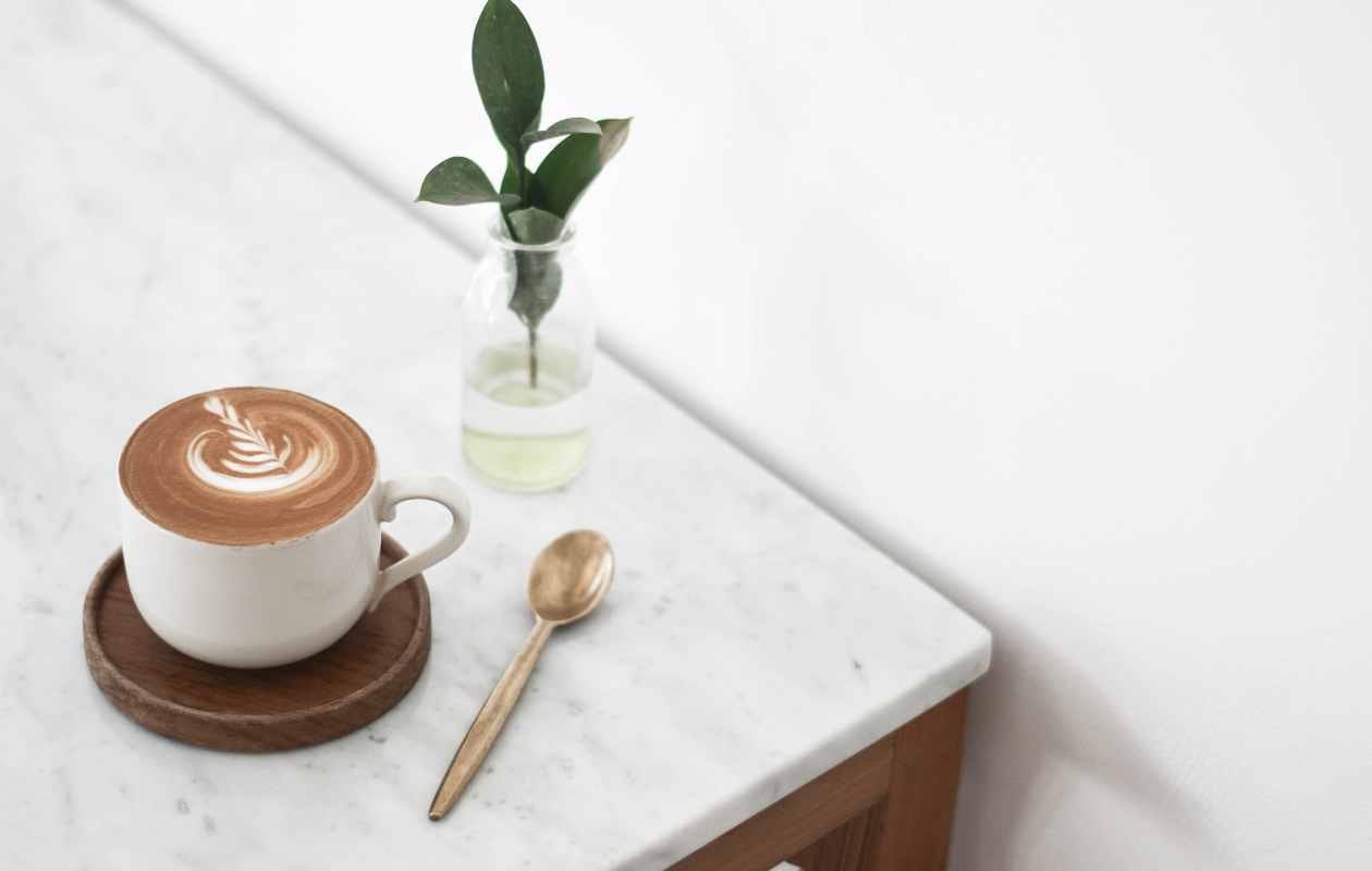 Taza de café con latte art sobre mesa de mármol con una cuchara y un pequeño jarrón decorativo - Memento Coffee