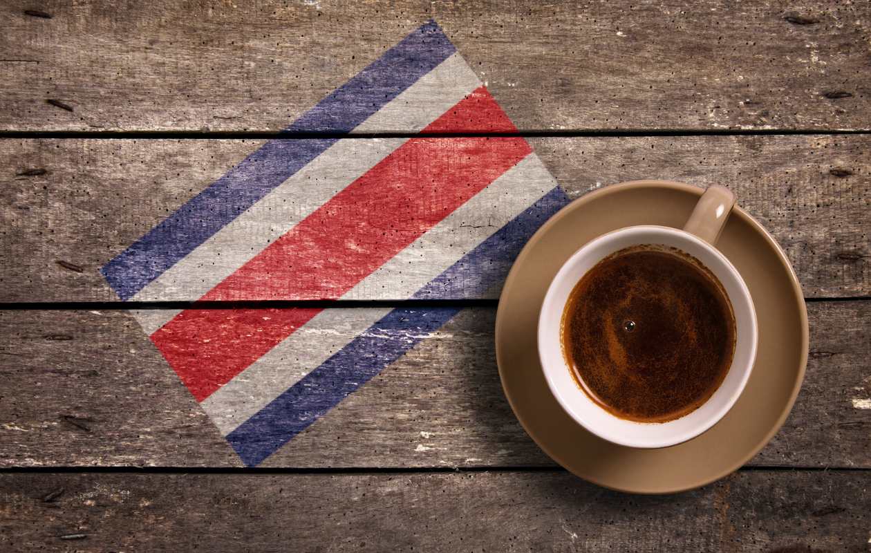 Taza de café sobre mesa de madera junto a la bandera de Costa Rica - Memento Coffee
